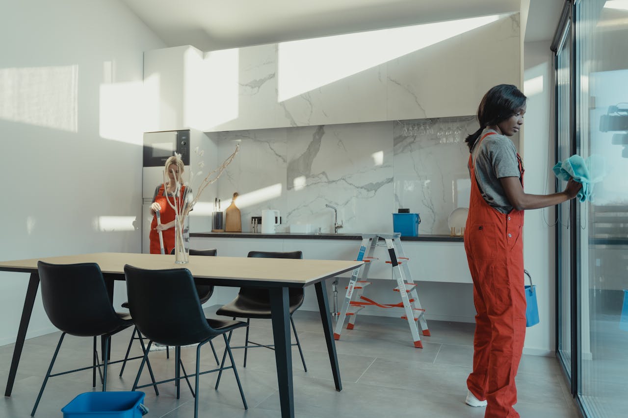 gallery-6 Two women in work clothes cleaning a kitchen with glass doors.