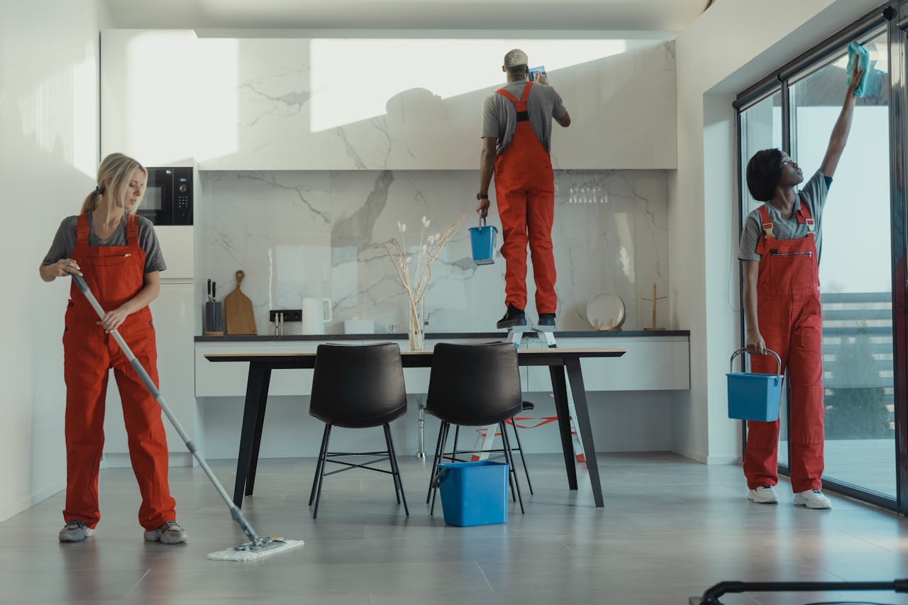 hero-img-02 Group of cleaners in red uniforms mopping and wiping glass in a modern dining room.